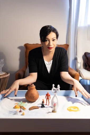 Laura Leite no consultório, diante de uma caixa de areia com miniaturas usadas em terapia