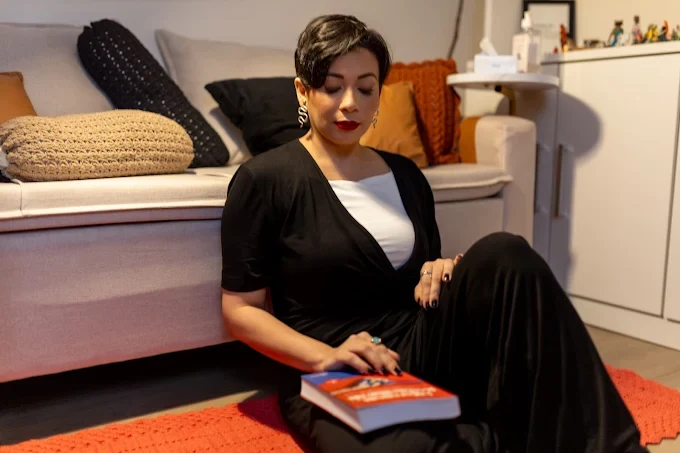 Laura Leite sentada no tapete do consultório, ao lado do sofá, com seu livro nas mãos